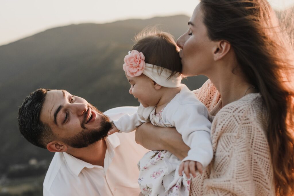 A joyful family moment with parents and baby enjoying the outdoors at sunset.
